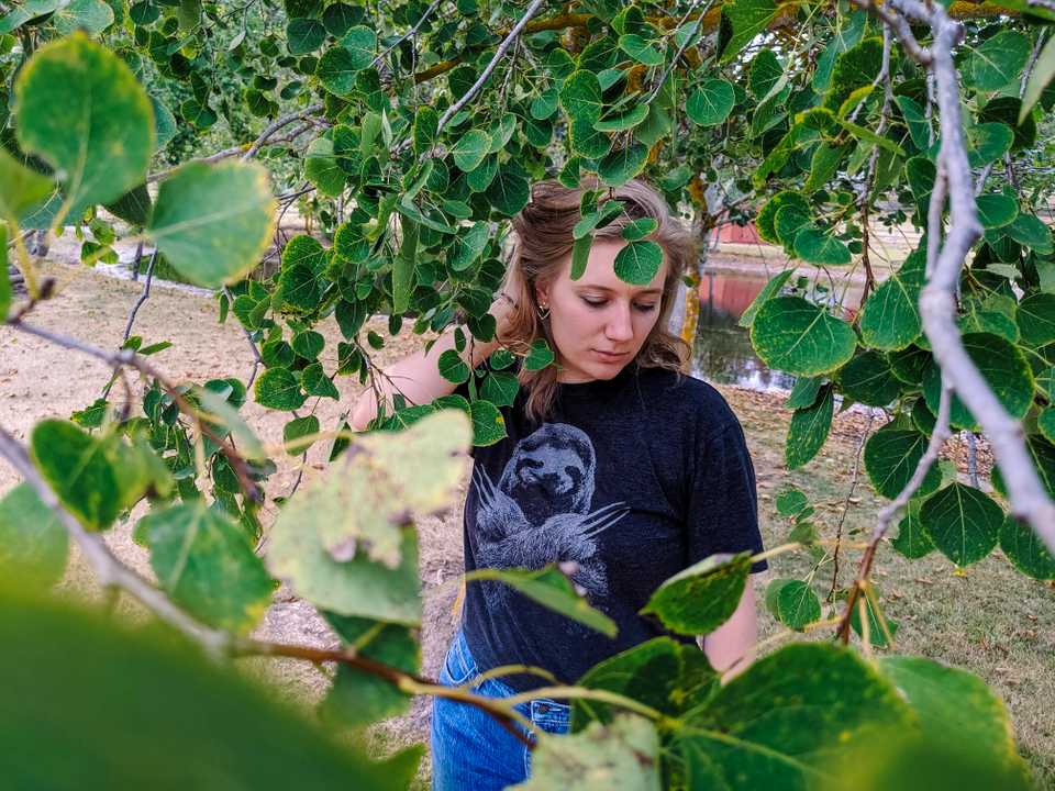 Hannah Donor amidst green leaves and wearing a dark grey sloth t-shirt and denim mom jeans