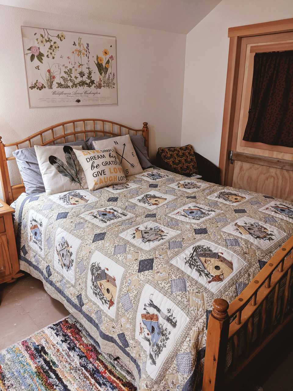 Rustic bed with handmade neutral birdhouse and birds quilt and art from Skagit County Tulip Festival on wall in barn loft bedroom